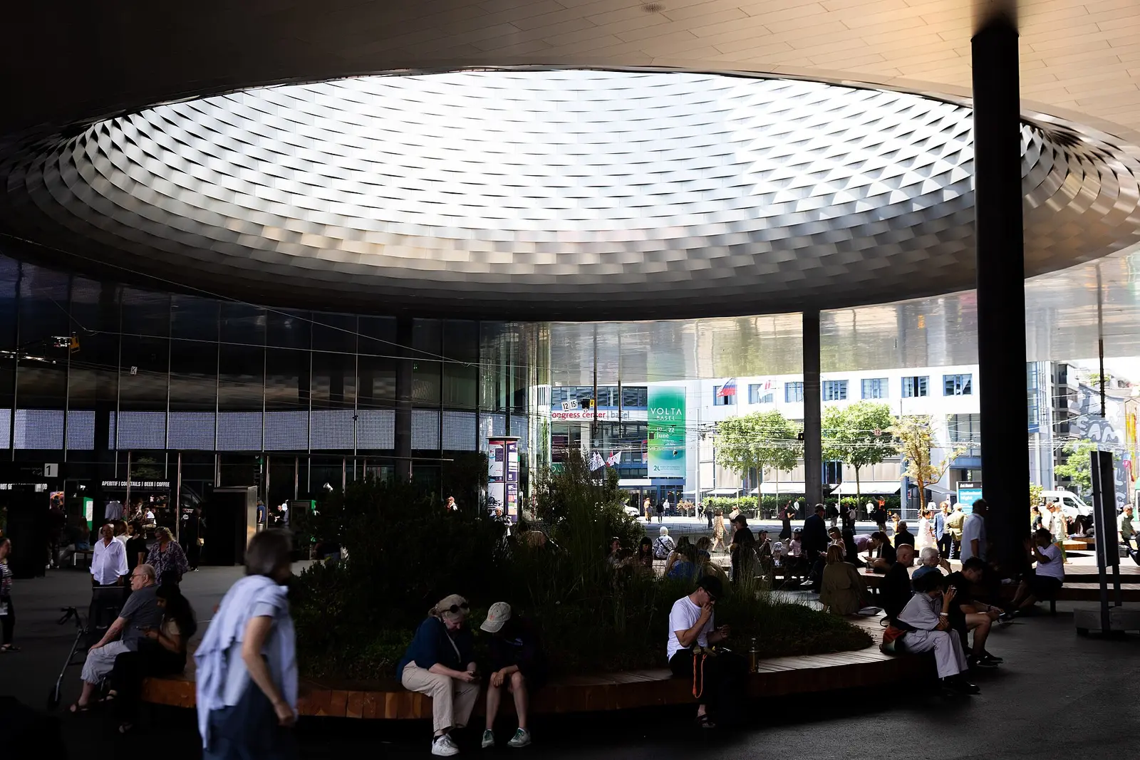 Visitors sit under the round roof opening at Messe Basel during Art Basel 2025
