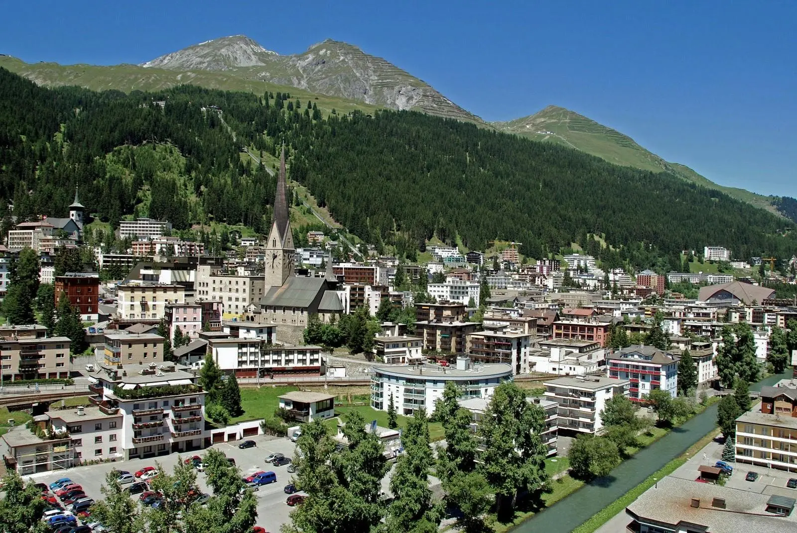 Davos town with church tower below forested mountains