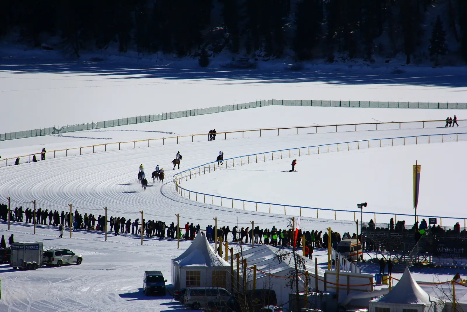 Horses racing on the snow covered frozen lake at St. Moritz with spectators along the rail and white tents